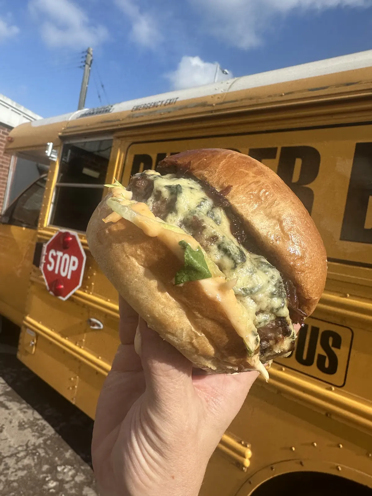 A Burger Bus beef burger held up in front of the bus